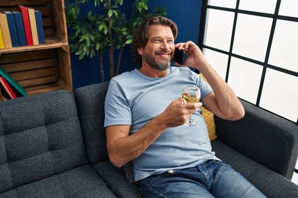 Orta Yaşlı Bir Adam Akıllı Telefondan Konuşuyor Evde Şarap Içiyor — Stok fotoğraf