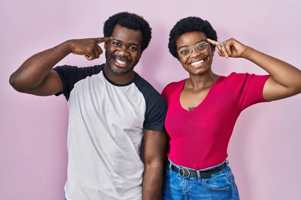 一对年轻的非洲裔美国夫妇站在粉红的背景上微笑着指指点点头 伟大的想法或想法 美好的回忆 — 图库照片