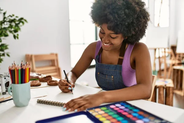 年轻的非洲裔美国女人坐在艺术工作室的桌子上 脸上挂着自信的笑容 — 图库照片