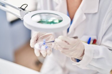 Young beautiful hispanic woman scientist holding flowers with tweezer at laboratory