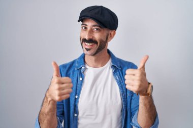 Arka planda sakallı İspanyol bir adam izole edilmiş başarı işaretinin üzerinde duruyor. Elleriyle olumlu jest yapıyor, gülümsüyor ve mutlu. Neşeli ifade ve kazanan jest. 