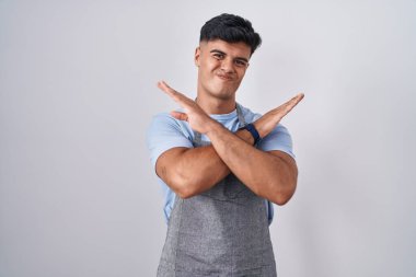 Beyaz arka planda önlük takan İspanyol genç adam reddedilme ifadesi kollarını kavuşturarak negatif işaret veriyor, kızgın surat. 