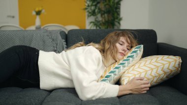 Young blonde woman lying on sofa sleeping at home