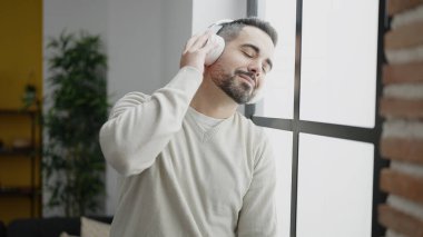 Young hispanic man listening to music standing at home