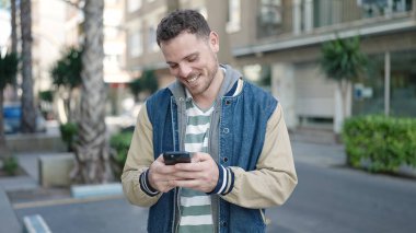 Young caucasian man smiling using smartphone at street