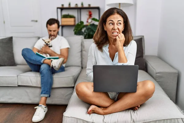 西班牙裔中年夫妇在家里 使用笔记本电脑的女人看上去很紧张 双手放在咬指甲的嘴上 焦虑问题 — 图库照片