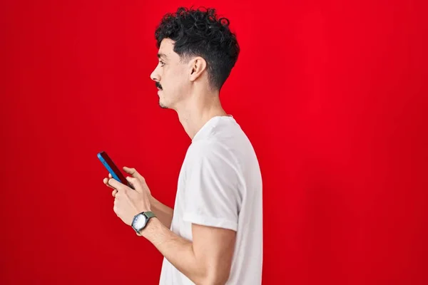 Hombre Hispano Usando Teléfono Inteligente Sobre Fondo Rojo Mirando Hacia — Foto de Stock