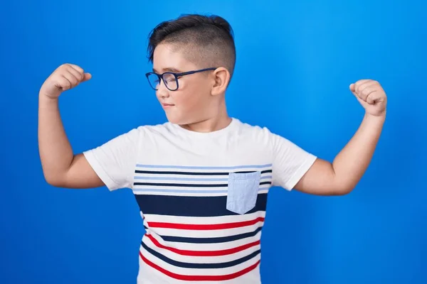 Joven Niño Hispano Pie Sobre Fondo Azul Mostrando Los Músculos —  Fotos de Stock