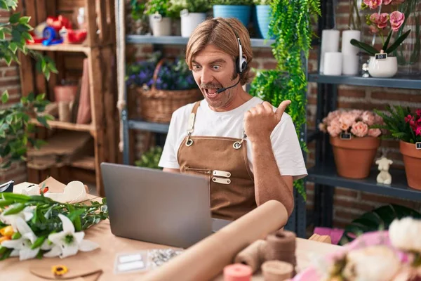 Caucasian man with mustache working at florist shop doing video call pointing thumb up to the side smiling happy with open mouth