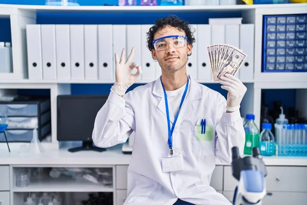 在科学家实验室工作的西班牙裔人拿着钱 手拿着手签 微笑着表示友善的手势 表示出极好的象征 — 图库照片