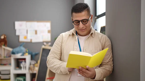 Young Hispanic Man Preschool Teacher Reading Book Standing Kindergarten — Stock fotografie