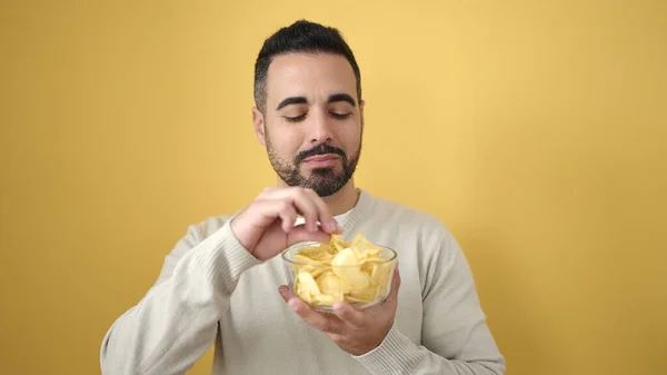 Young Hispanic Man Smiling Confident Eating Chips Potatoes Isolated Yellow — Stock Photo, Image