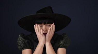 Siyah arka plan üzerinde korku ifadesi olan cadı kostümü giyen genç Çinli kadın.