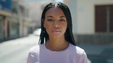 Afro-Amerikalı kadın gülümsüyor. Kollarını kavuşturup caddede duruyor.