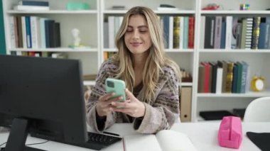 Young blonde woman student using computer and smartphone studying at library university