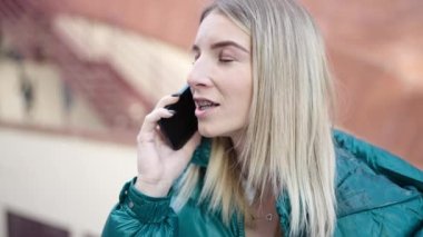 Genç sarışın kadın caddede telefonla konuşuyor.