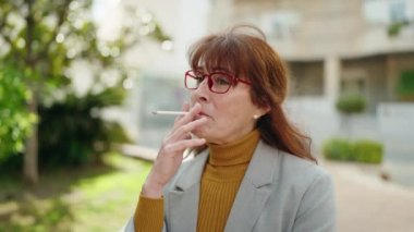 Middle age woman business executive smoking cigarette at park