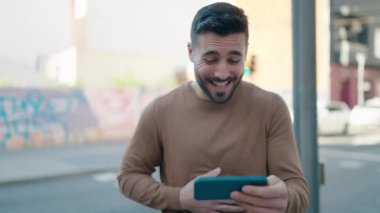 Young hispanic man watching video on smartphone at street
