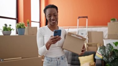 Afro-Amerikalı kadın yeni evinde akıllı telefon paketi kullanıyor.