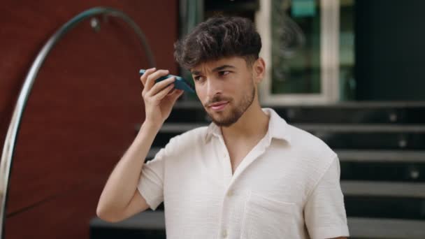 Молодий Арабський Чоловік Посміхається Впевнено Слухаючи Аудіоповідомлення Телефону Вулиці — стокове відео