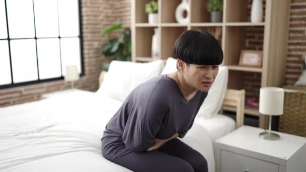 若いです中国人女性苦しみのために月経痛座っています上のベッドルーム — ストック動画