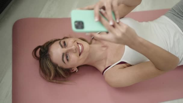 Jonge Blonde Vrouw Met Behulp Van Smartphone Liggend Yoga Mat — Stockvideo