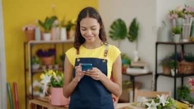 Young african american woman florist smiling confident using smartphone at flower shop