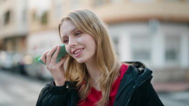 Young blonde girl smiling confident listening audio message by the smartphone at street