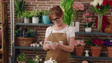 Middle age woman florist smiling confident using smartphone at flower shop