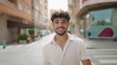 Genç Arap adam sokakta yürürken kendinden emin gülümsüyor.