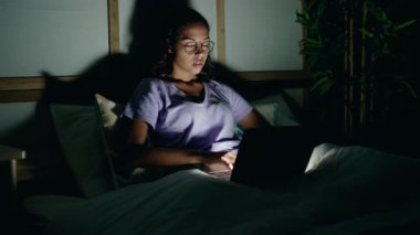 Genç Afrikalı Amerikalı kadın dizüstü bilgisayar kullanıyor. Yatak odasında otururken yorgun.