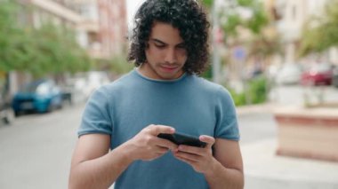 Sokakta video oyunu oynarken kendinden emin gülümseyen genç Latin adam.