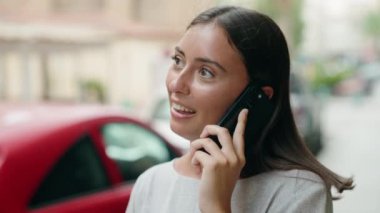 Genç, güzel, İspanyol bir kadın gülümsüyor ve caddede akıllı telefondan konuşuyor.