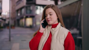 Genç sarışın kadın gülümsüyor. Kendine güveni tam. Akıllı telefondan konuşuyor.