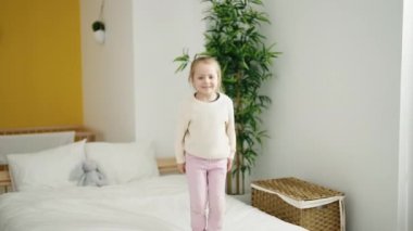 Adorable blonde girl smiling confident jumping on bed at bedroom