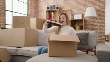 Genç sarışın kadın gülümsüyor. Kendine güvenen boks ayakkabılarını yeni evinde pakette açıyor.