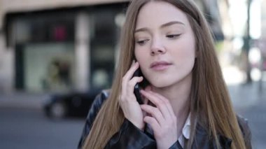 Young blonde woman talking on smartphone with serious expression at street