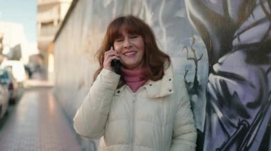 Middle age redhead woman smiling confident talking on the smartphone at street
