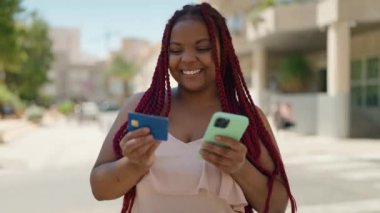 African american woman using smartphone and credit card at street