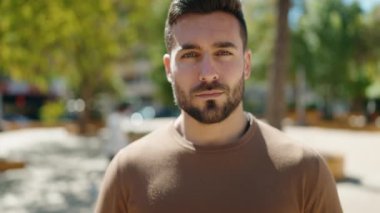 Genç İspanyol adam gülümsüyor. Parkta kollarını kavuşturmuş duruyor.