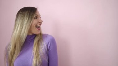 Young blonde woman standing with surprise expression pointing up with fingers over isolated pink background
