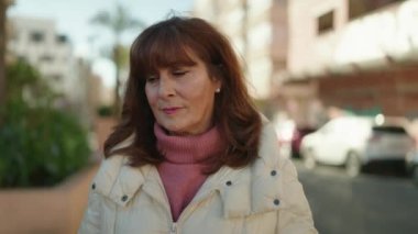 Orta yaşlı, yüzü rahat bir şekilde caddede duran kızıl saçlı kadın.