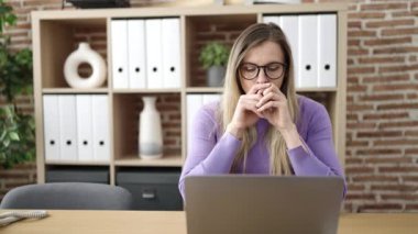 Genç sarışın iş kadını ofiste şüpheli bir ifadeyle dizüstü bilgisayar kullanıyor.