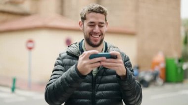 Young man smiling confident watching video on smartphone at street