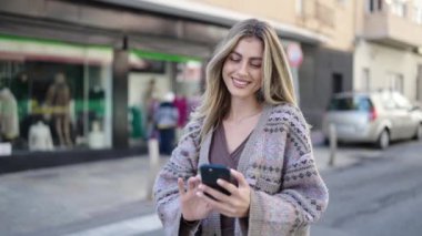 Young blonde woman smiling confident making selfie by the smartphone at street