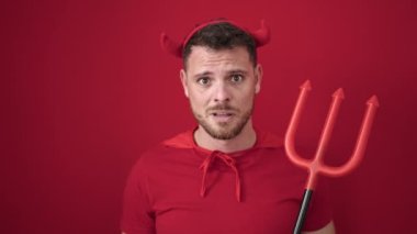 Young caucasian man looking afraid wearing devil costume over isolated red background