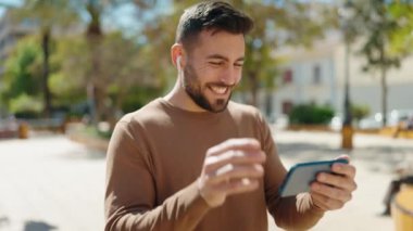 Genç İspanyol adam parkta akıllı telefondan video izliyor.