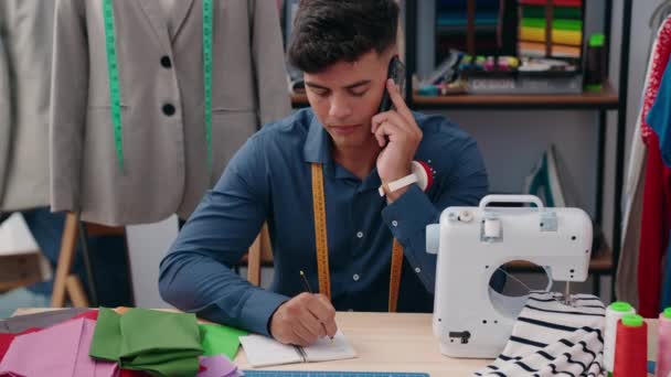在服装厂 他的年轻人裁缝正在谈论在笔记本上写智能手机 — 图库视频影像