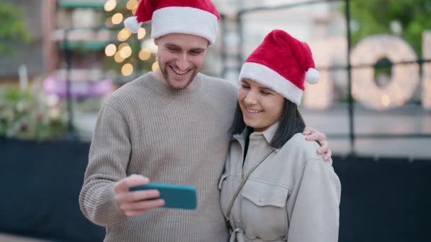 Νεαρό Ζευγάρι Φοράει Χριστουγεννιάτικο Καπέλο Χρησιμοποιώντας Smartphone Στο Πάρκο — Αρχείο Βίντεο