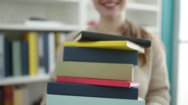 Kütüphane üniversitesinde elinde kitaplarla gülümseyen sarışın genç bir kız.